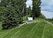 Thumbnail 37 of 39 - A green sign with white text on a grassy hill.