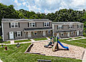 Thumbnail 23 of 39 - A playground area with a slide and a sandbox in front of a building.