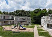 Thumbnail 22 of 39 - A playground with a slide and a bench in the foreground and apartment buildings in the background.