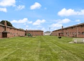 Thumbnail 14 of 25 - brick apartment building with a grassy field in front of it