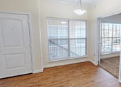 Thumbnail 9 of 32 - A room with a white door, a window with blinds, and a wooden floor.