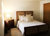 Thumbnail 12 of 35 - a bedroom with a bed with white bedding and a nightstand with a lamp on it