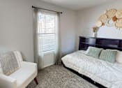 Thumbnail 11 of 29 - A white chair sits in a bedroom with a bed and a window with curtains.