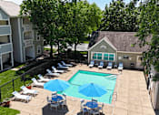 Thumbnail 18 of 29 - A pool surrounded by chairs and umbrellas with trees and a building in the background.