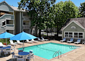 Thumbnail 15 of 29 - A pool surrounded by chairs and umbrellas in front of apartment buildings.