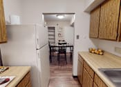 Thumbnail 4 of 36 - A kitchen with a white refrigerator, wooden cabinets, and a dining table with chairs.