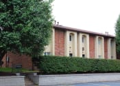 Thumbnail 27 of 31 - a large brick building with a hedge in front of it