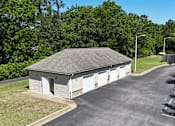 Thumbnail 23 of 27 - A small building with a grey roof and white doors is surrounded by a parking lot.