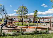 Thumbnail 12 of 16 - A playground with a slide, swings, and sandbox in front of a residential area.