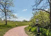 Thumbnail 9 of 16 - A path in a park with a sign on the right.