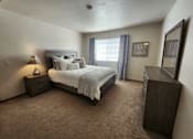 Thumbnail 10 of 28 - A bedroom with a large bed and a nightstand with a lamp.