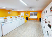 Thumbnail 24 of 30 - A laundromat with rows of washing machines and a fan on the ceiling.