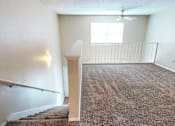 Thumbnail 13 of 30 - A room with a carpeted floor and a staircase leading to another room.
