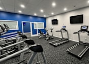 Thumbnail 16 of 26 - A gym with treadmills, exercise bikes, and a television.