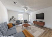 Thumbnail 2 of 29 - A living room with a grey couch, a wooden coffee table, a flat screen TV, and a ceiling fan.