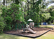Thumbnail 18 of 26 - A playground with a slide and swings surrounded by trees.