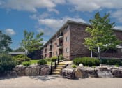 Thumbnail 24 of 28 - a brick apartment building with a stone retaining wall and landscaping
