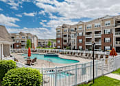 Thumbnail 21 of 29 - A white fence surrounds a pool in front of apartment buildings.
