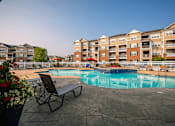 Thumbnail 22 of 29 - A pool area with a chair and a bench in front of apartment buildings.