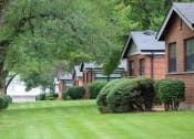 Thumbnail 11 of 16 - a row of apartments on a green lawn with trees and bushes
