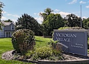 Thumbnail 25 of 35 - A sign for Victorian Village Rental Townhomes is surrounded by shrubbery.