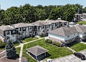 Thumbnail 29 of 33 - Apartment complex with a mix of brick and siding exteriors, surrounded by a green lawn and trees.