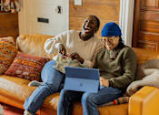 Thumbnail 5 of 8 - Two people sitting on a couch with a laptop.