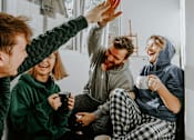 Thumbnail 3 of 8 - Four people in pajamas are sitting on a couch, laughing and holding mugs.