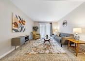 Thumbnail 9 of 35 - A living room with a grey couch, a wooden coffee table, and a painting on the wall.