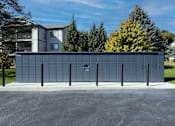 Thumbnail 31 of 35 - A large grey building with a blue door in the middle of a paved area.