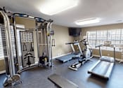 Thumbnail 16 of 19 - A gym with a variety of equipment including treadmills, weights, and a television.