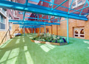 Thumbnail 11 of 19 - a patio with green grass and a flower bed in front of a brick building