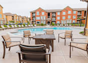 Thumbnail 19 of 22 - A pool surrounded by chairs and tables in front of apartment buildings.