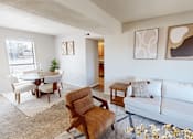 Thumbnail 2 of 31 - A living room with a white couch, a brown chair, and a small table with a plant on it.