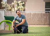 Thumbnail 34 of 93 - A man kneeling on the ground with his dog.at Copper Creek Apartments, Las Vegas, NV