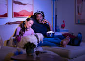 Thumbnail 21 of 93 - A man and woman are sitting on a couch with a dog between them, both wearing headphones and looking at a tablet.at Copper Creek Apartments, Las Vegas, 89123