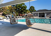 Thumbnail 16 of 39 - Two hanging chairs over a pool with a house in the background.