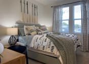 Thumbnail 16 of 42 - Luxury Apartments in Myrtle Beach, SC, With In-Unit Washer and Dryer - Anchor Pointe - Cozy Bedroom With Upholstered Bed, Patterned Bedding, Bedside Lamp, Wall Decor, and Windows With Curtains.
