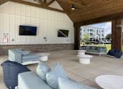 Thumbnail 3 of 42 - Pet-Friendly Luxury Apartments In Myrtle Beach, SC - Anchor Pointe - A Large Covered Outdoor Lounge With Light Blue Sofas, Bean Bags, And Wall-Mounted Televisions.