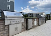 Thumbnail 5 of 42 - Dog-Friendly Luxury Apartments in Myrtle Beach, SC - Anchor Pointe - Outdoor Grilling Station With Stainless Steel Gas Grills, Brick Counter, Fenced Patio Pathway, and Overlooking Apartment Homes.