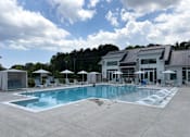 Thumbnail 1 of 42 - 2-Bedroom Luxury Apartments in Myrtle Beach, SC - Anchor Pointe - Resort-Style Swimming Pool With In-Water Loungers, Sun Deck Chairs, Umbrella Seating, White Cabanas, and Clubhouse Building.