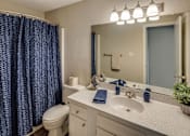 Thumbnail 12 of 15 - A bathroom with a white sink, toilet, and a blue shower curtain at River Ridge Apartments in Asheville, NC