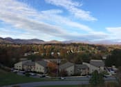 Thumbnail 15 of 15 - A large building complex with a parking lot in front of it at River Ridge Apartments in Asheville, NC