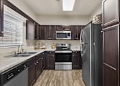 Thumbnail 7 of 19 - A kitchen with dark wood cabinets and stainless steel appliances at Heights at New Garden apartments in Greensboro, NC.