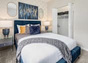 Thumbnail 23 of 27 - A bedroom with a large bed, nightstands with lamps and a closet door open.
