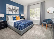Thumbnail 22 of 27 - A bedroom with a large bed, a chair, a nightstand, and a large window with curtains.