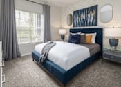 Thumbnail 24 of 27 - A bedroom with a large bed, pillows, nightstands with lamps, and a large window with grey curtains hanging.