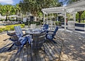 Thumbnail 13 of 27 - Outdoor wooden deck with blue chairs in a circle and a white pergola in the background.