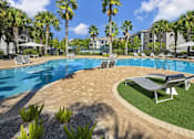 Thumbnail 10 of 27 - A swimming pool surrounded by palm trees and lounge chairs with a circle of green grass.