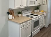 Thumbnail 5 of 15 - A white kitchen with a stove, oven, and microwave.